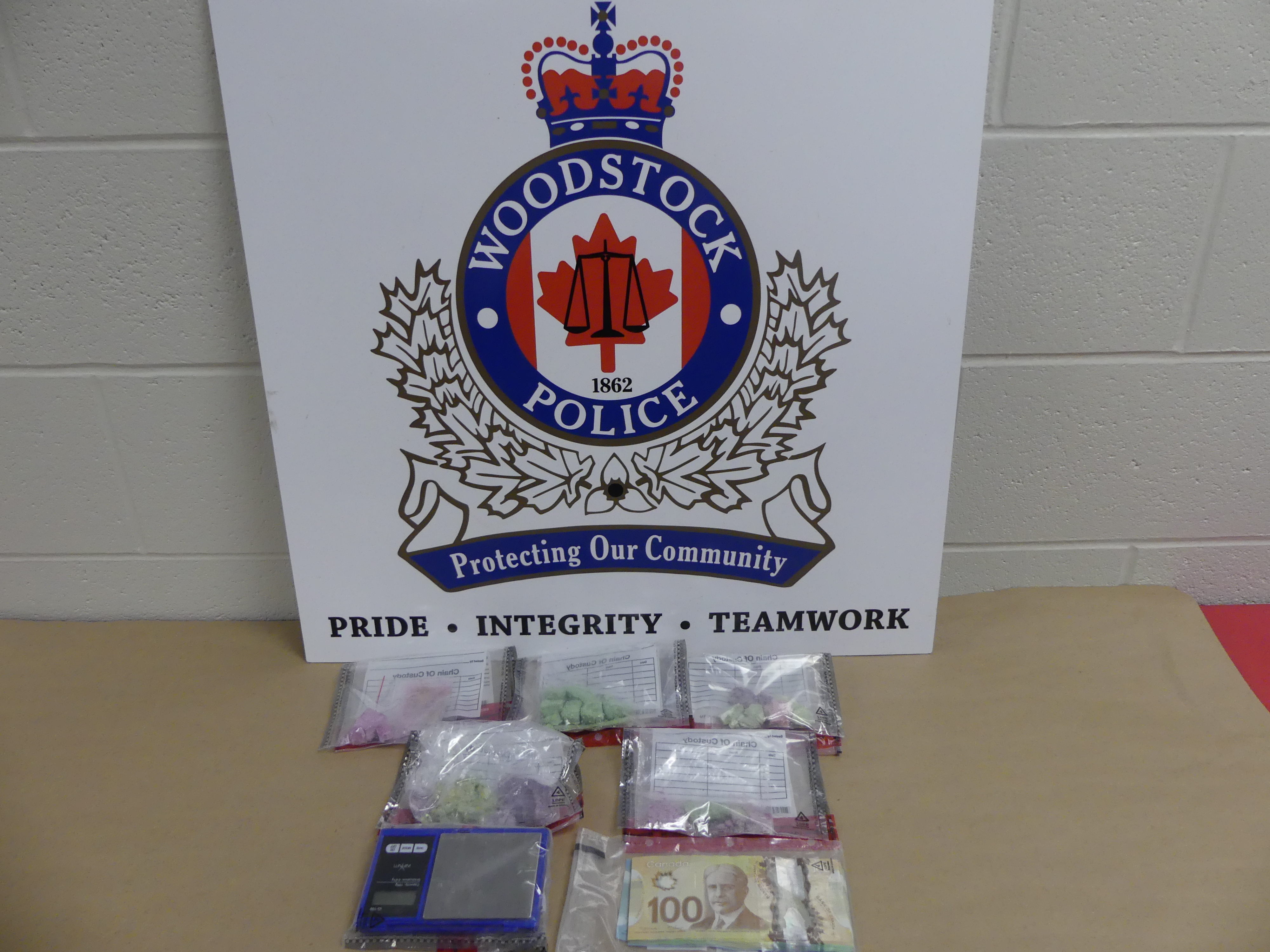 Woodstock Police Logo with packages of drugs, a scale and cash in bags in front of the logo